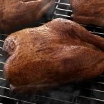 Three SADLER'S SMOKEHOUSE® whole turkeys smoking on a rack.