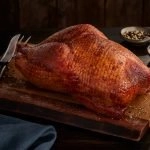 A SADLER'S SMOKEHOUSE® whole turkey on a cutting board with seasonings in the background.